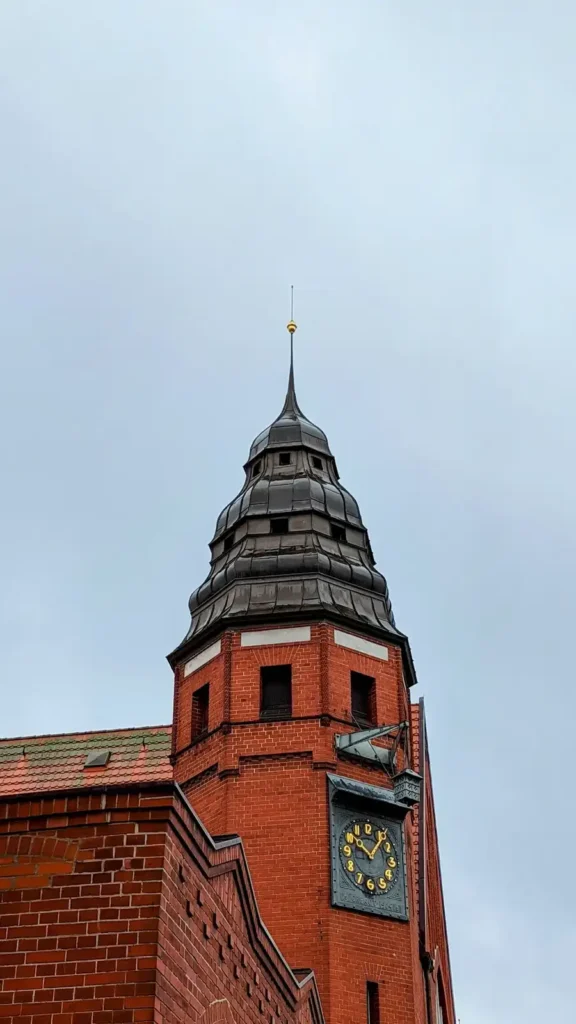 Turm des Hauptbahnhofs Stralsund aus rotem Backstein mit Uhr und dunkler Haube