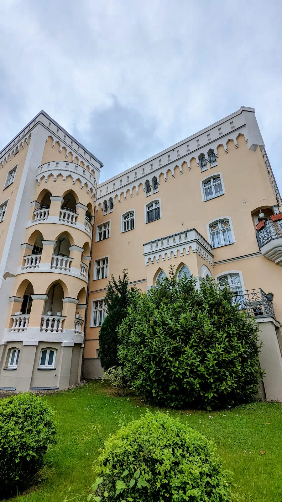 Das sogenannte Schloss am Sund in Stralsund, ein heller Bau mit Zinnen, Rundbogenfenstern und Balkonen, davor Rasen und Büsche