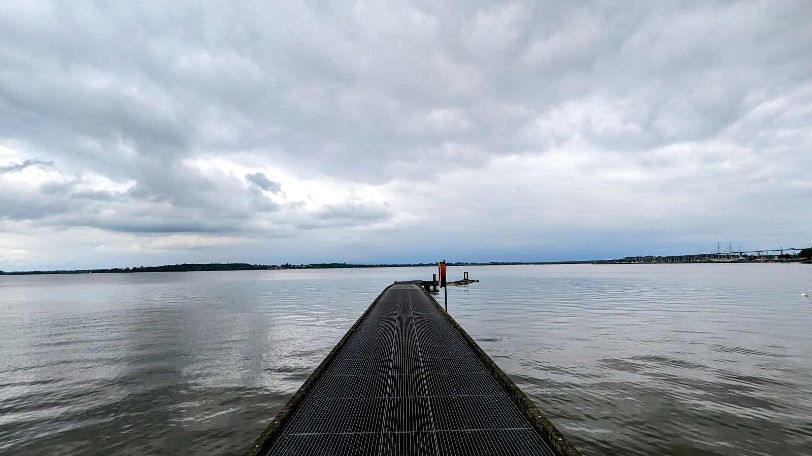 Steg aus Gitterrost an der Sundpromenade in Stralsund, dahinter der Strelasund unter bewölktem Himmel