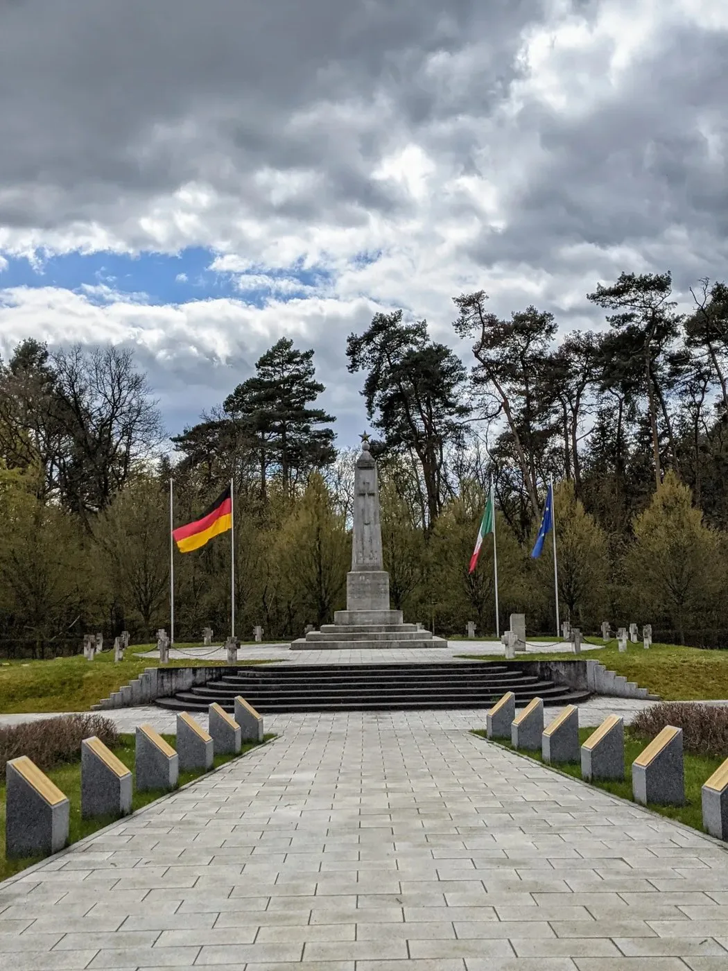 Plattenweg zu einem Denkmal mit Stufen und Fahnen, seitlich Grabsteine