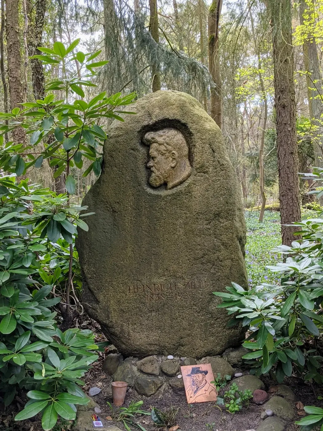 Findling mit eingearbeitetem Reliefkopf eines Mannes zwischen Rhododendren