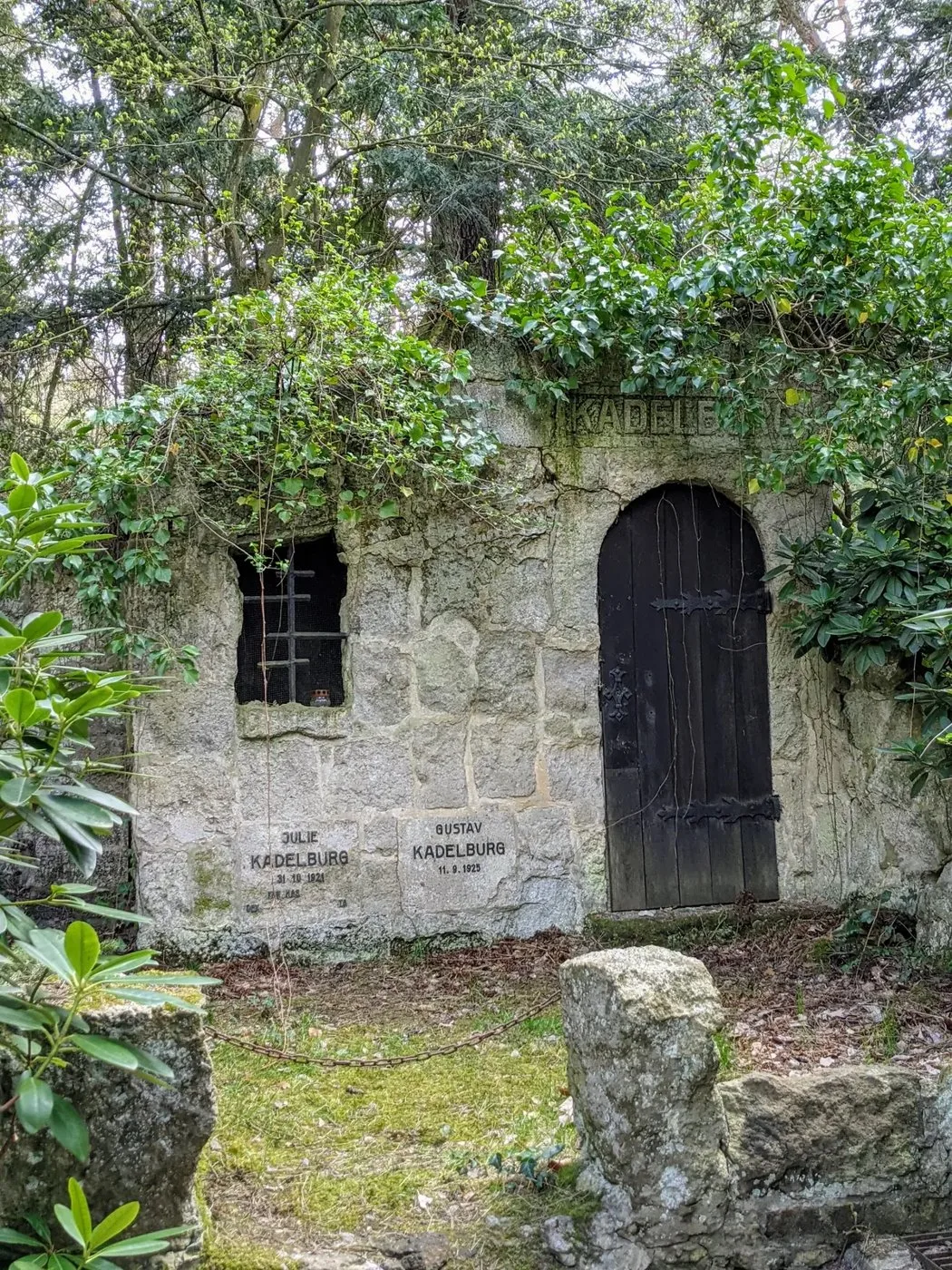 Überwachsene Gruft aus Naturstein mit Holztür und vergittertem Fenster