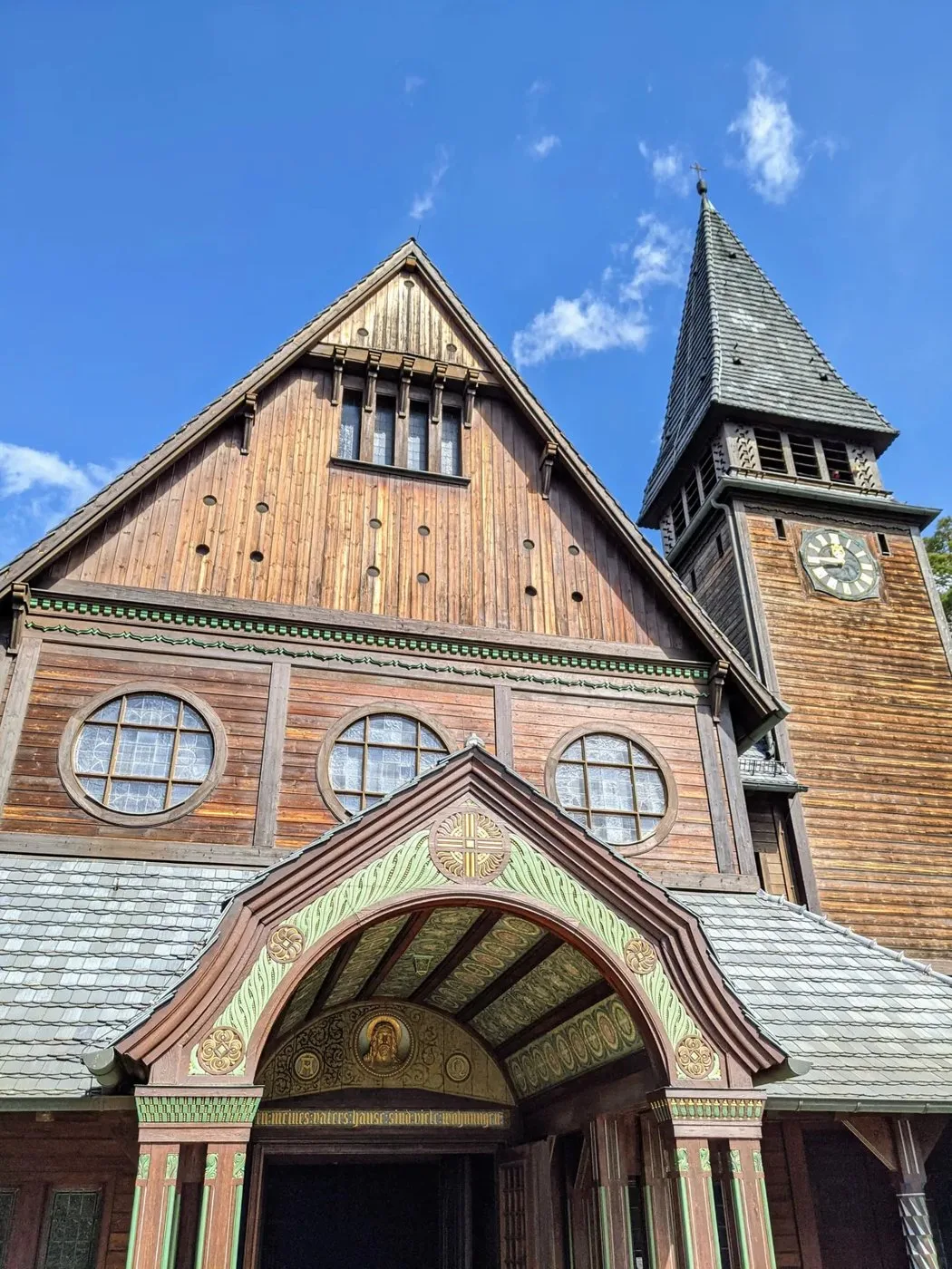 Eingangsseite der Holzkapelle mit Rundfenstern, Uhrturm und bemaltem Vorbau