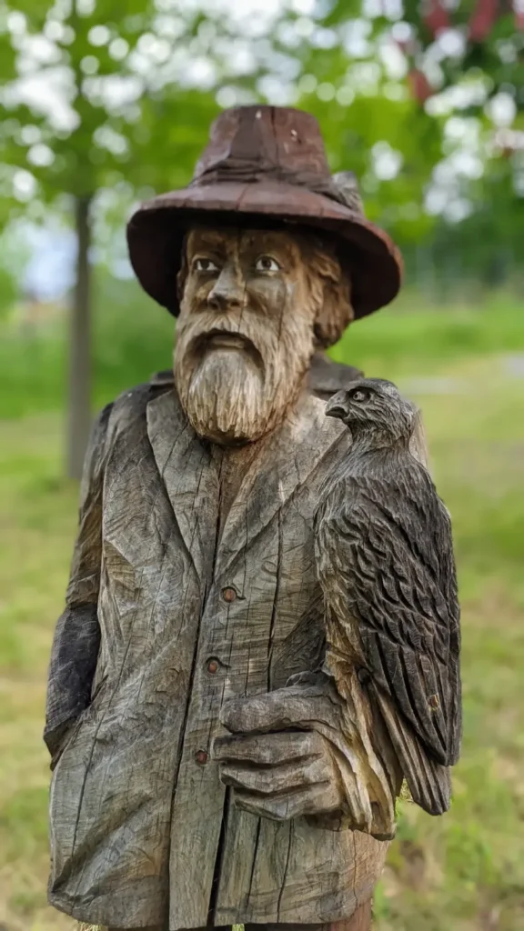 Holzfigur eines bärtigen Mannes mit Hut und Greifvogel auf dem Arm