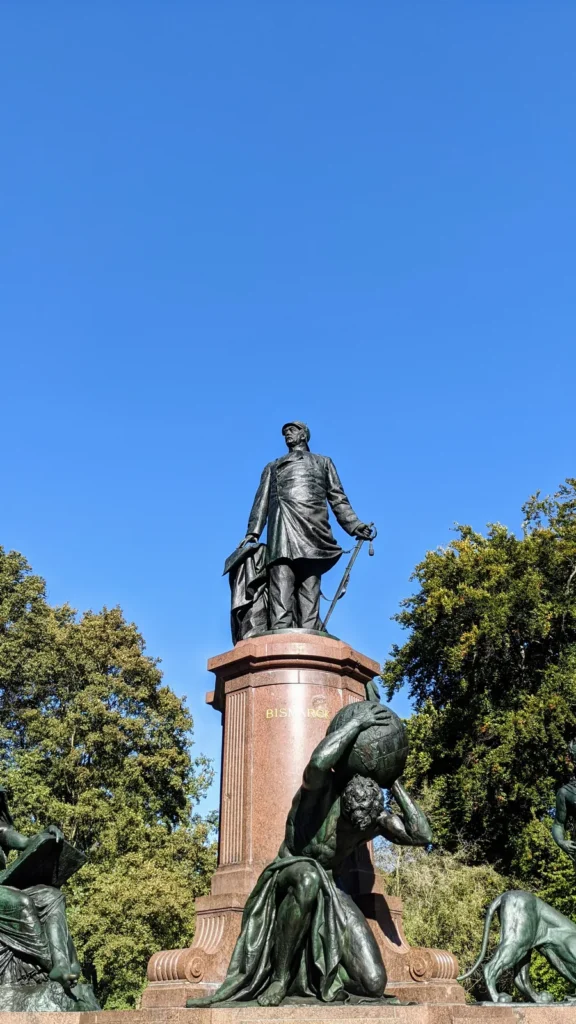 Bronzefigur Bismarcks auf rotem Granitsockel am Großen Stern, davor allegorische Figuren