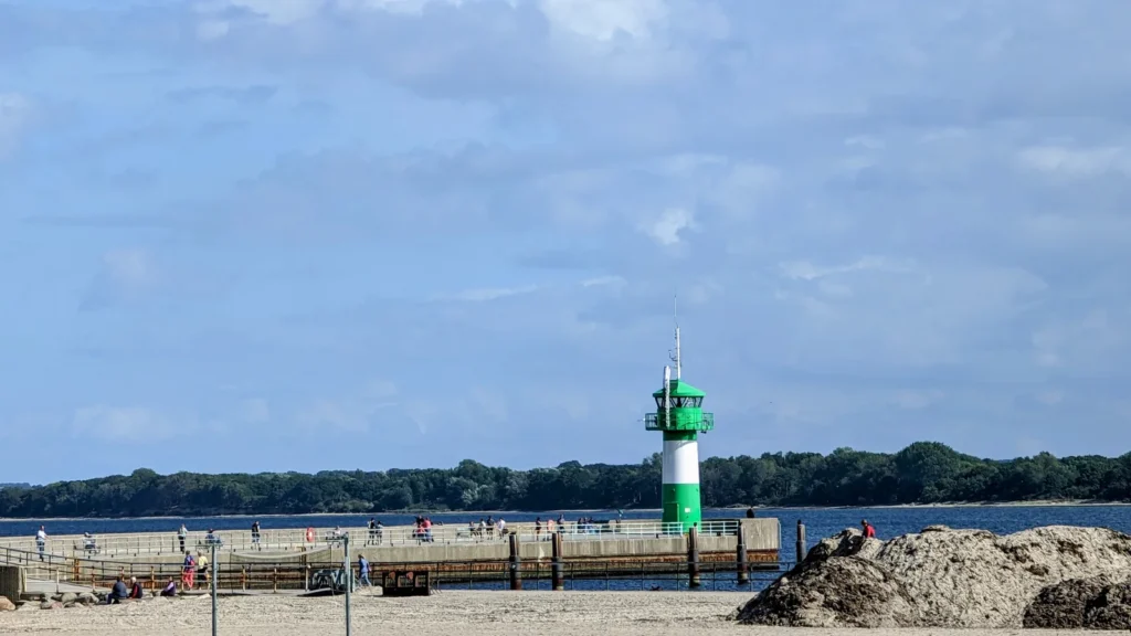 Grün-weißes Leuchtfeuer auf einer Mole vor bewaldetem Ufer in Travemünde