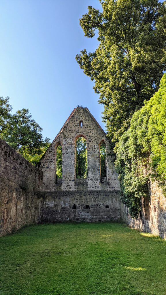 Giebelwand einer Kirchenruine aus Feldstein mit drei Fensteröffnungen, davor Rasen