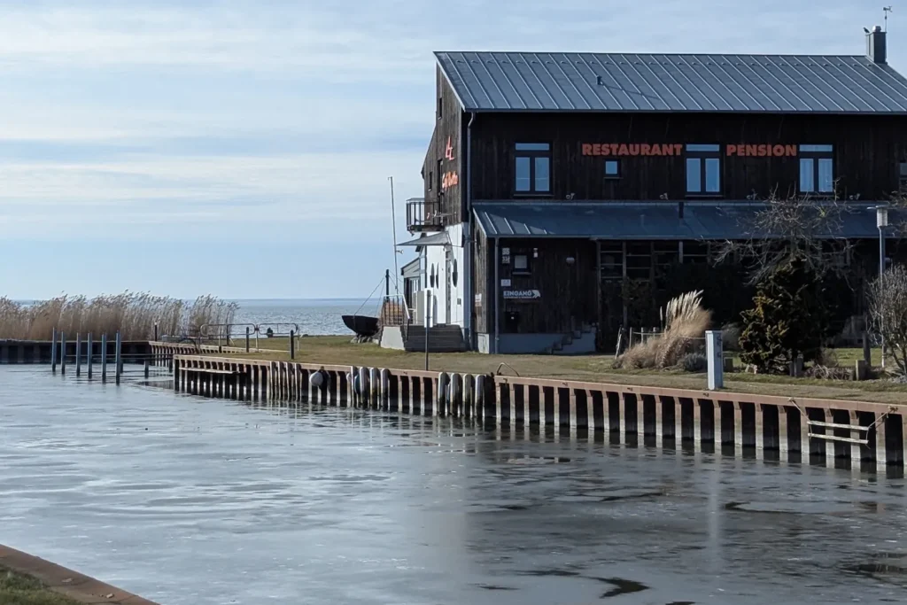 Zugefrorenes Hafenbecken in Ückeritz mit dunklem Holzhaus am Achterwasser
