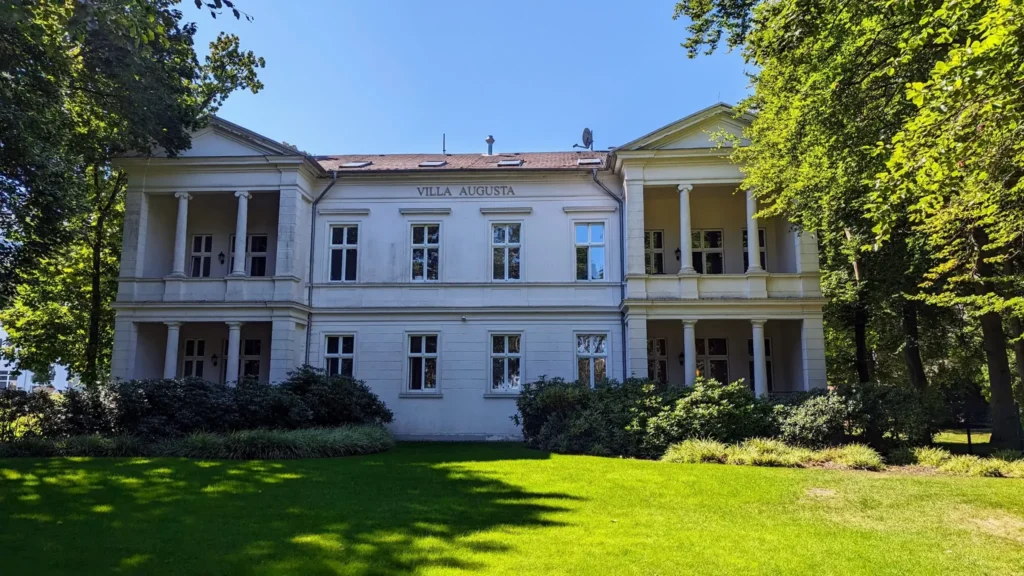 Villa Augusta in Heringsdorf, ein weißer Bau mit zwei Loggienflügeln hinter einer Wiese