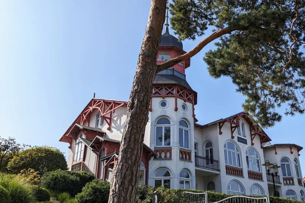 Villa mit rotem Fachwerk und Turm an der Strandpromenade von Zinnowitz, davor eine Kiefer