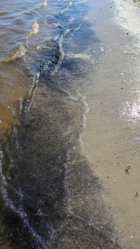Flache Wellen laufen über den nassen Sand am Spülsaum