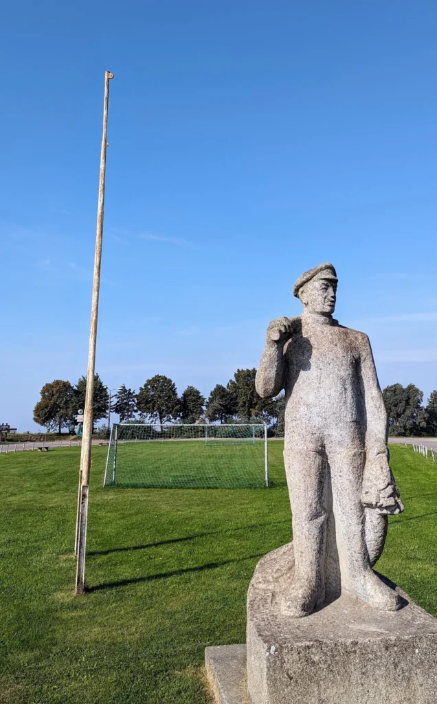 Steinfigur eines Fischers mit Mütze am Rand eines Sportplatzes in Kamminke