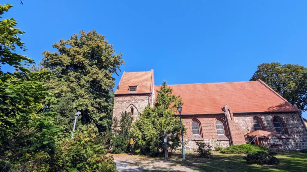 Backsteinkirche von Koserow mit Feldsteinsockel und kurzem Turm zwischen Bäumen