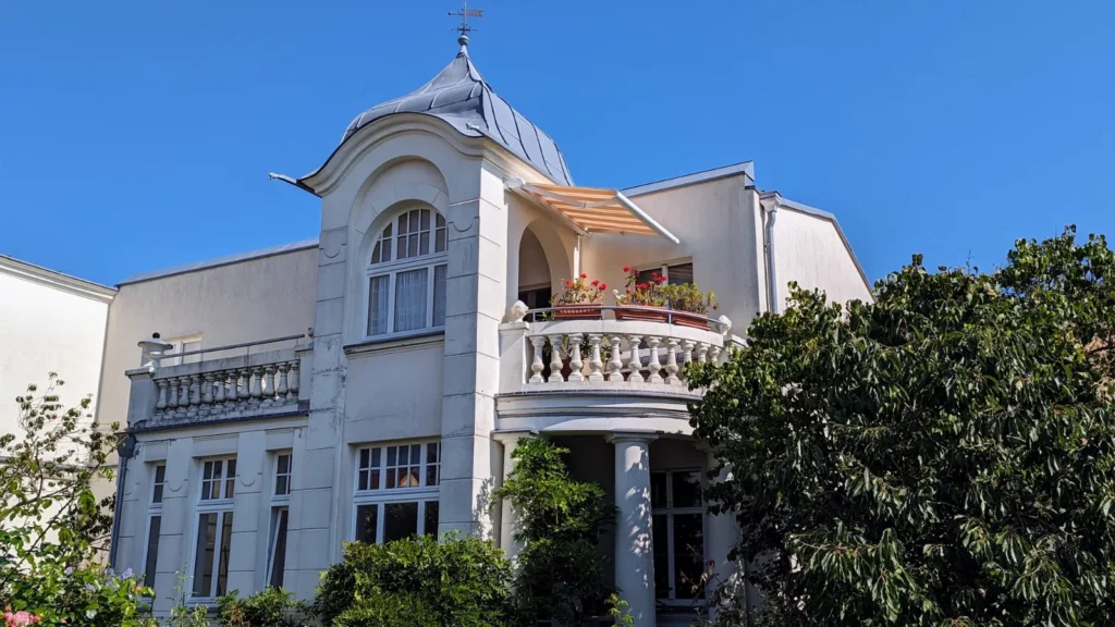 Weiße Villa mit Balkonen und geschwungener Turmhaube an der Hauptstraße in Koserow