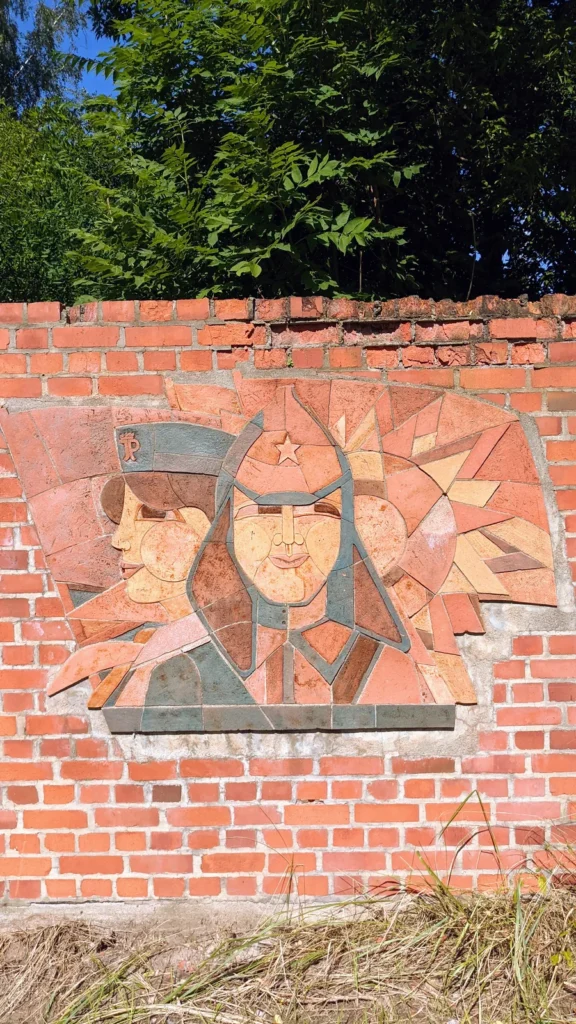 Relief aus rötlichen Fliesen mit zwei Köpfen an einer Ziegelmauer bei Hindenburg