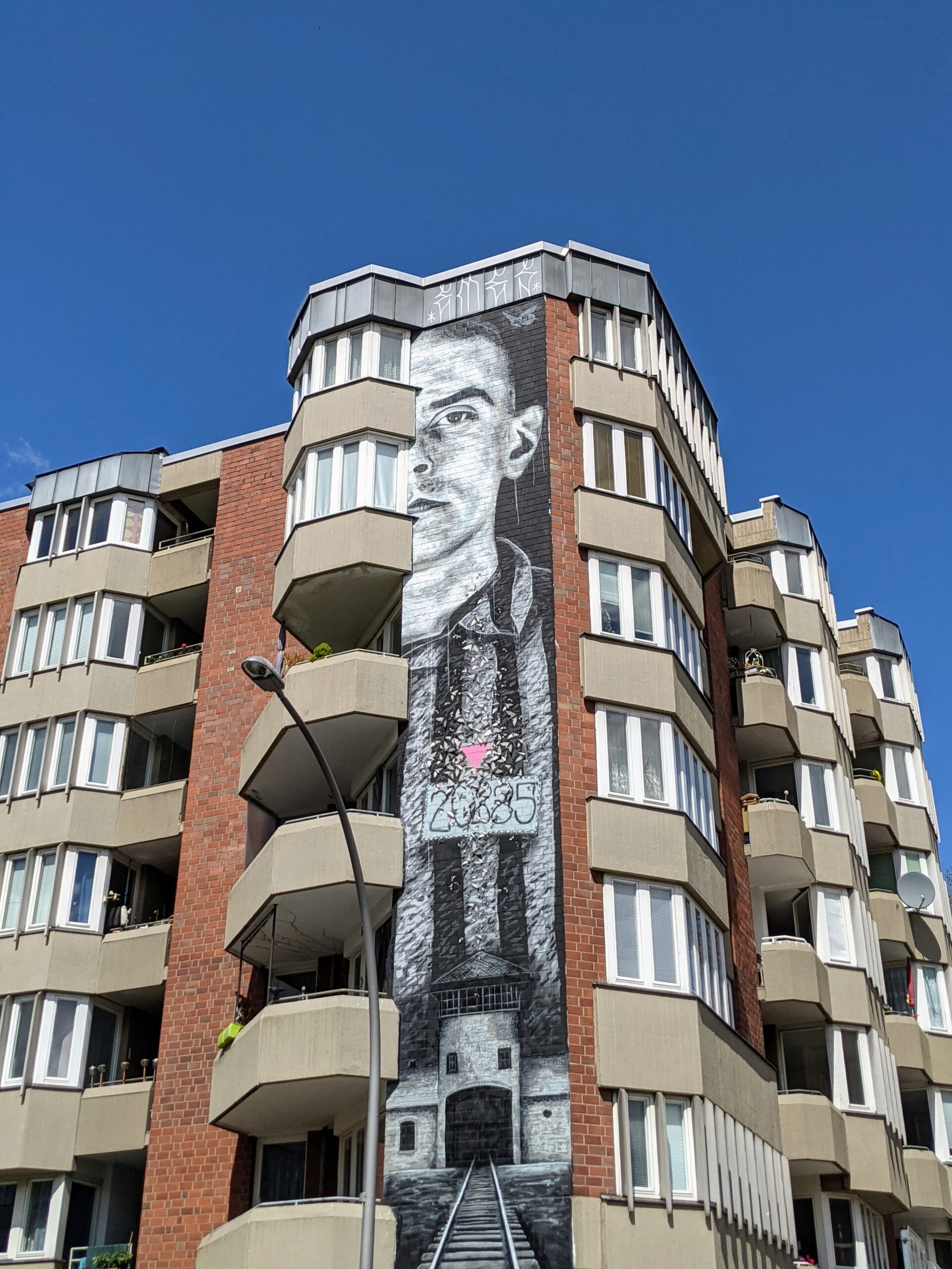 Porträt von Walter Degen als Wandbild von Nils Westergard an der Ecke eines Wohnhauses in der Bülowstraße, unten ein Bahngleis und ein Torhaus