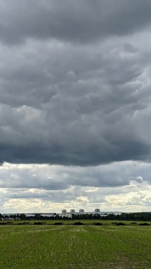 Dunkle Wolken über einem Feld der Wartenberger Feldmark, am Horizont die Häuser der Stadt