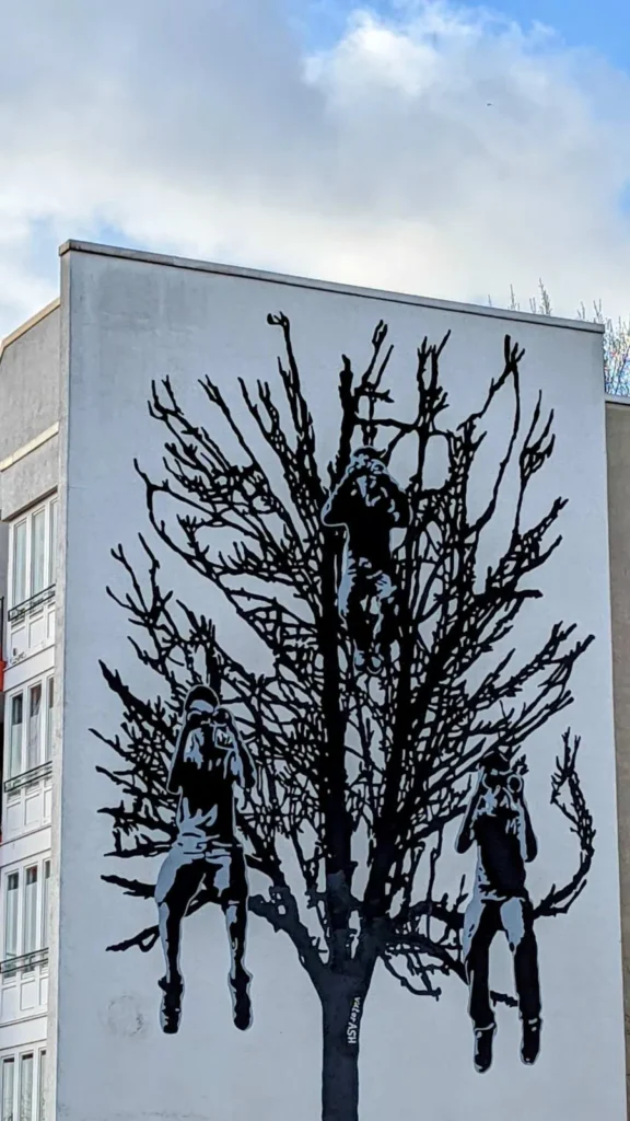 Wandbild Tree Children von Victor Ash: schwarzer Baum mit drei Kindern an einer Brandwand