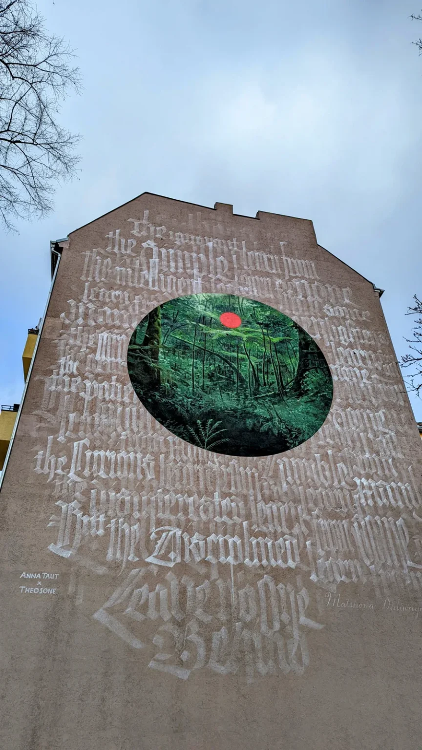Brandwand in der Kameruner Straße mit rundem Waldbild in Grün und Kalligrafie in Frakturschrift