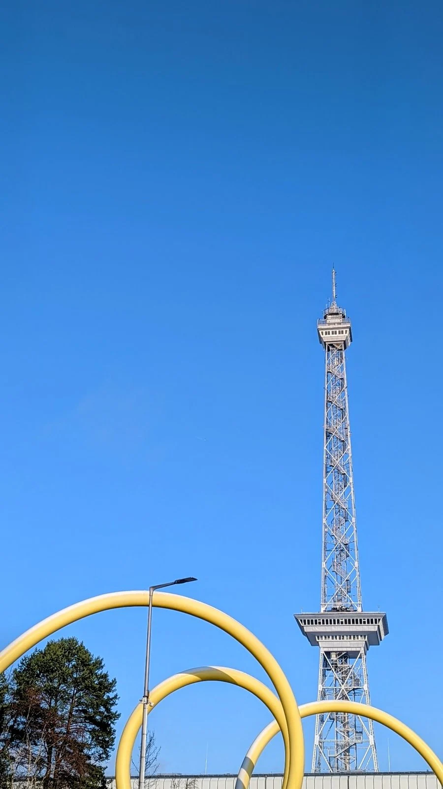 Funkturm auf dem Messegelände in Westend, davor gelbe Bögen vor blauem Himmel