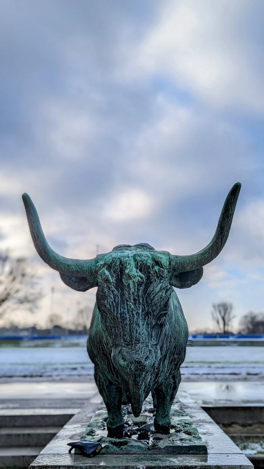 Bronzestier auf einem Sockel am Sportforum im Olympiagelände Westend, dahinter ein Spielfeld