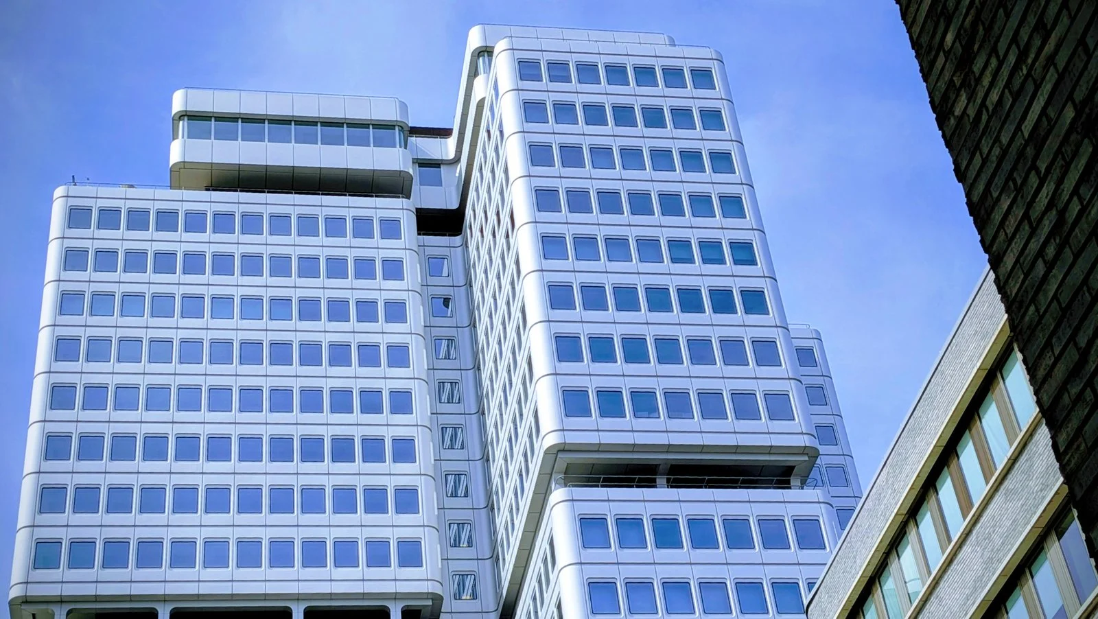 Gestaffelter weißer Hochhausbau mit Glasfassade in Wilmersdorf vor blauem Himmel