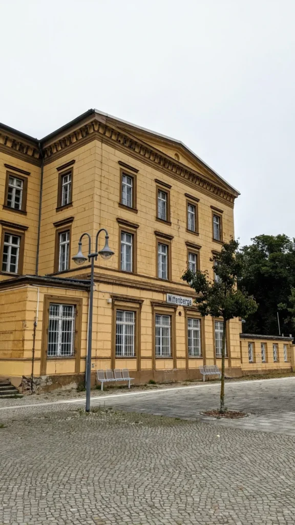 Ockergelbes Bahnhofsgebäude mit Laterne und Kopfsteinpflaster davor in Wittenberge