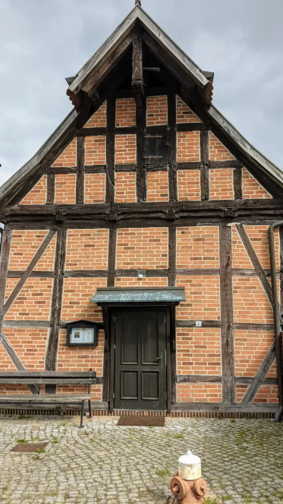 Fachwerkgebäude mit Backsteinfeldern und dunkler Tür, davor Kopfsteinpflaster in Gnevsdorf