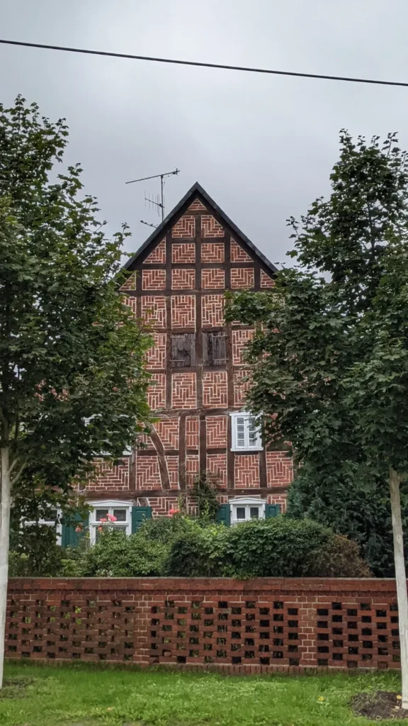 Fachwerkgiebel hinter zwei Bäumen und einer durchbrochenen Backsteinmauer in Zwischendeich bei Wittenberge