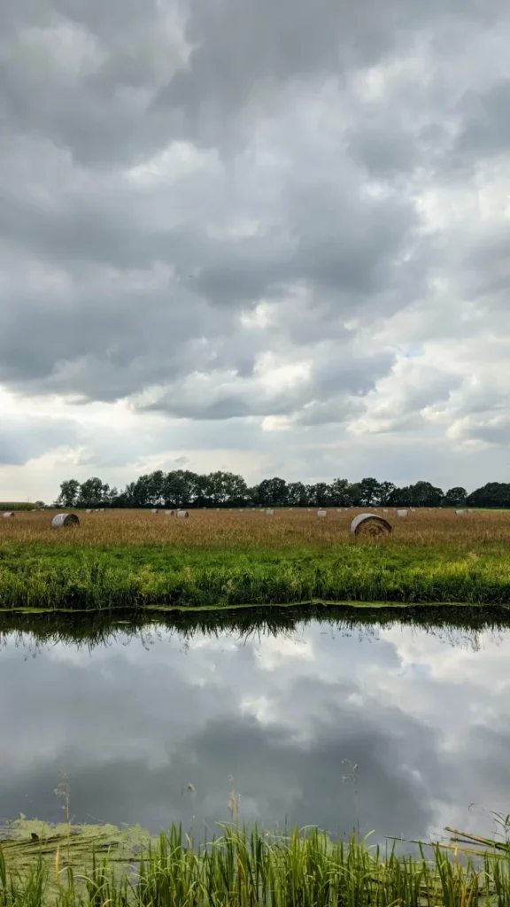 Kanal mit Strohballen auf dem Feld dahinter unter dunklen Wolken bei Bad Wilsnack in der Prignitz