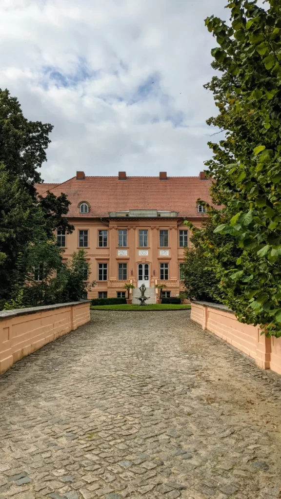Kopfsteinpflasterzufahrt zum Schloss Rühstädt mit rotem Dach