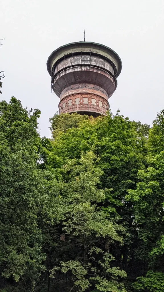 Runder Backsteinwasserturm mit weit auskragendem Wasserbehälter über Baumkronen in Wittenberge