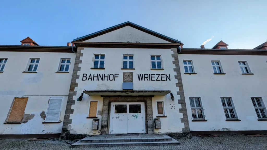 Weißes, zweigeschossiges Empfangsgebäude mit dem Schriftzug Bahnhof Wriezen über dem Eingang, einige Fenster im Erdgeschoss sind verschlossen
