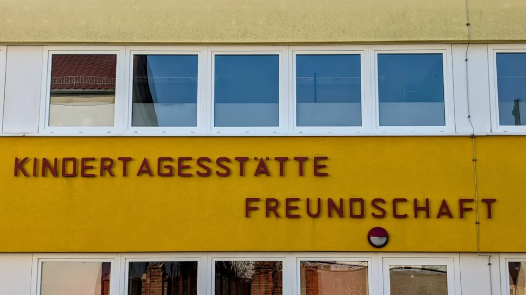 Gelbe Fassade mit dem Schriftzug Kindertagesstätte Freundschaft in roten Buchstaben zwischen zwei Fensterbändern