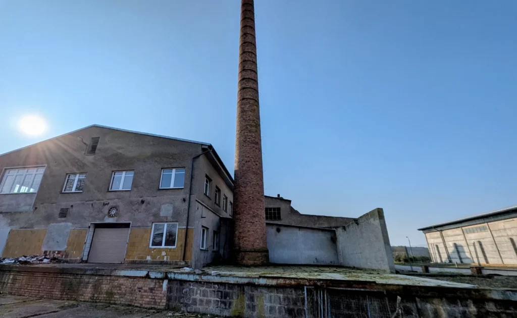 Graues Fabrikgebäude mit hohem Backsteinschornstein und Laderampe am alten Hafen in Wriezen