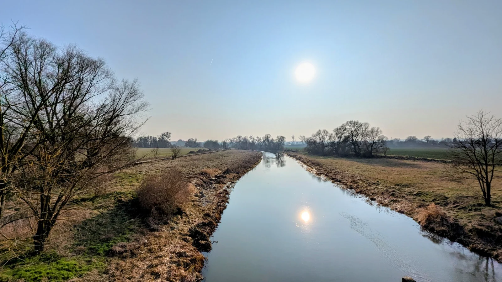 Blick von der Brücke bei Neugaul auf die Wriezener Alte Oder, die tief stehende Sonne spiegelt sich im ruhigen Wasser zwischen flachen Ufern
