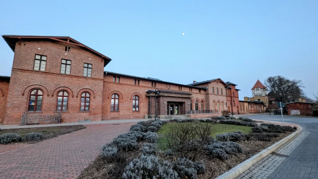 Langgestrecktes Empfangsgebäude aus rotem Backstein am Bahnhof Bad Freienwalde, im Hintergrund der Wasserturm mit Fachwerkaufsatz