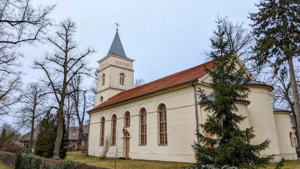 Dorfkirche Wünsdorf, heller Saalbau mit Turm, zwischen kahlen Bäumen