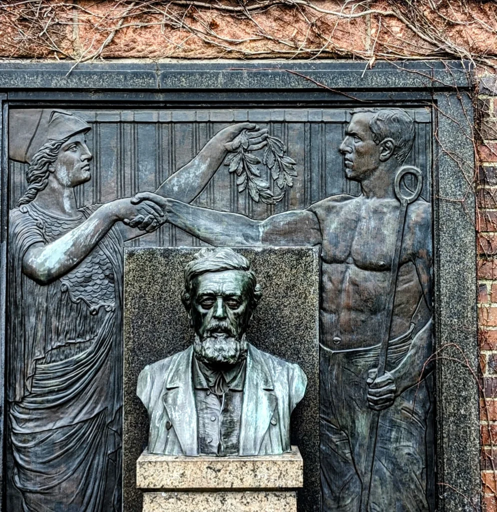Grabmal an der Ringmauer der Gedenkstätte der Sozialisten mit Bronzebüste und Relief, auf dem eine Frauengestalt und ein Arbeiter einander die Hand reichen