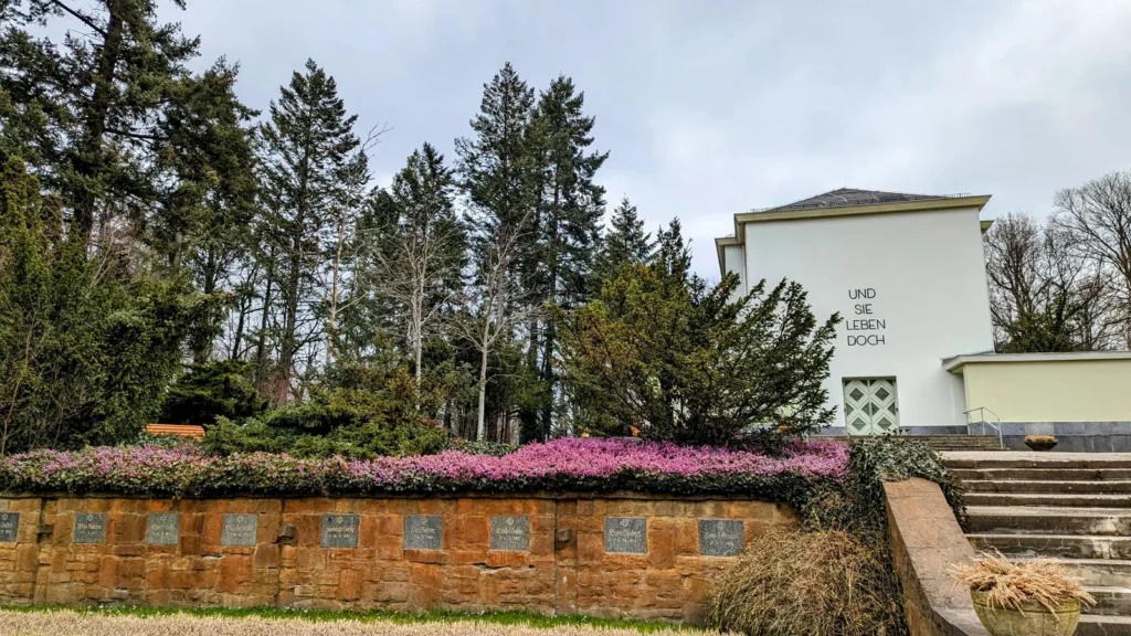 Blick über die Urnengräber am Pergolenweg zur weißen Feierhalle des Zentralfriedhofs Friedrichsfelde